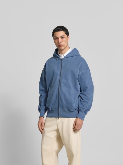 Männermodel trägt Oversized Sweatjacke aus Baumwolle von ANNARR in Blau mit Zweiwege-Reißverschluss, Balloon-Look, elastische Abschlüsse, Ganzkörperansicht von vorne. Rückenlänge 73 cm, Schulterbreite 48 cm, Ärmellänge 74 cm bei Größe M.