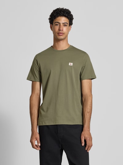 Mannenmodel draagt Regular Fit T-Shirt aus reiner Baumwolle van Calvin Klein Jeans in effen kaki, ronde hals, korte mouwen, label patch, katoenstructuur, regular fit. Ganzkörperansicht van voren.