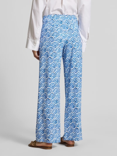 Frauenmodel trägt Wide Fit Stoffhose mit elastischem Bund von HERZENS, weiß-blaues Wellenmuster, Gehstoff, Gesäßtaschen, Ganzkörperansicht Rückansicht.