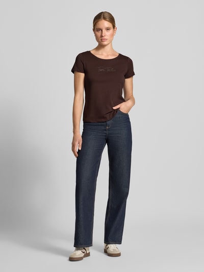Kobiece model prezentuje Damski t-shirt 'Regular Fit T-Shirt aus reiner Baumwolle' od Tom Tailor w kolorze brązowym, gładka faktura materiału, ciemnoniebieskie spodnie, neutralne tło, damski t-shirt od Tom Tailor, pełen widok z przodu.