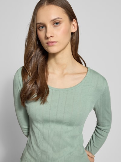 Frauenmodel trägt Slim Fit Langarmshirt aus Bio-Baumwoll-Mix Modell 'TENNA LIFE' von ONLY, Optik: unifarben, feines Lochstrickmuster, U-Boot-Ausschnitt, Ärmelabschluss und Rumpfabschluss mit Frill, Materialverarbeitung: Feinstrick, Nahaufnahme Oberkörper.