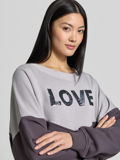 Frauenmodel trägt Oversized Sweatshirt aus reiner Baumwolle von miss goodlife mit Paillettenbesatz, zweifarbig grau und anthrazit, Nahaufnahme Oberkörper.