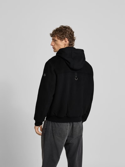 Männermodel trägt Jacke mit Kapuze von Moose Knuckles in Schwarz, Woll-Mix, Regular Fit, Pattentaschen, Ganzkörperansicht Rückansicht.
