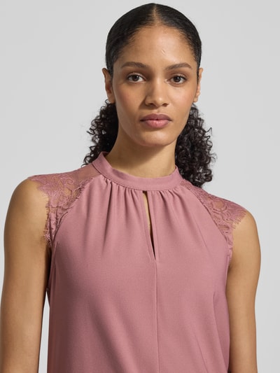 Vrouwenmodel draagt Regular Fit Blusentop met kant model 'MILLA' van Vero Moda in effen oudroze met staande kraag, kanten kapmouwen, sleutelhals op de rug, 2-knoopsluiting achter, detailopname bovenlichaam.
