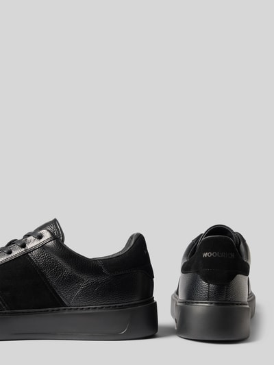 Produktfoto, Sneaker aus echtem Leder Modell 'Classic Court' von Woolrich in Schwarz mit strukturierter Sohle und Kontrastbesatz, seitliche und Rückansicht, Herren Sneaker, abgerundete Form, Schnürverschluss, Label-Schriftzug, Absatzhöhe 4 cm, Schafthöhe 8 cm, Schaftweite 9 cm.