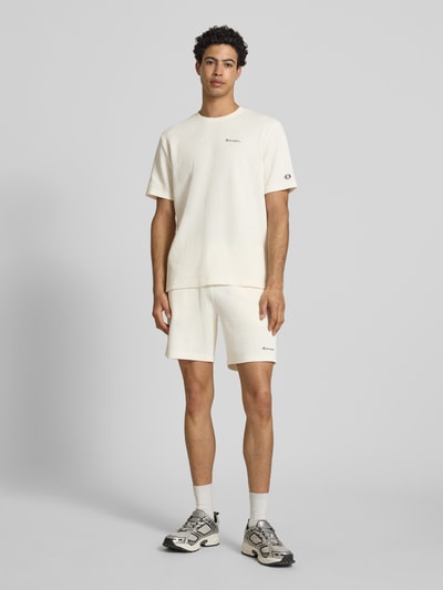 Männermodel trägt T-Shirt mit Strukturmuster und Label-Stitchings von CHAMPION, Baumwoll-Mix, Regular Fit, cremefarben, Ganzkörperansicht von vorne.