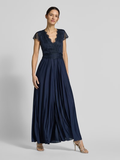 Modelka nosi wieczorową suknię z koronką Abendkleid mit Spitzenbesatz Modell 'Emelie' od GUIDO MARIA KRETSCHMER WOMAN, dopasowany krój, głęboki dekolt V, pasek w talii, kryjąca halka, długość z tyłu w rozmiarze 36: 40 cm, szerokość w rozmiarze 36: 33 cm, długość rękawa w rozmiarze 36: 13 cm, całkowita długość w rozmiarze 36: 148 cm, długość wewnętrzna nogawki w rozmiarze 36: 83 cm, granatowy kolor, zwiewny materiał, całofigurowe ujęcie z przodu.