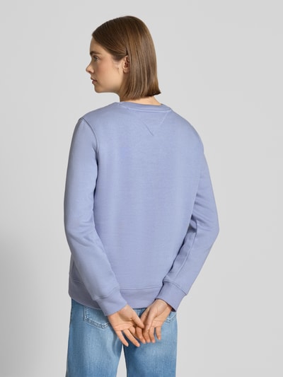 Modelka kobieca nosi Regular Fit Sweatshirt aus Baumwoll-Mix od Tommy Jeans w kolorze jasnofioletowym, gładka faktura, widok całej sylwetki z tyłu.