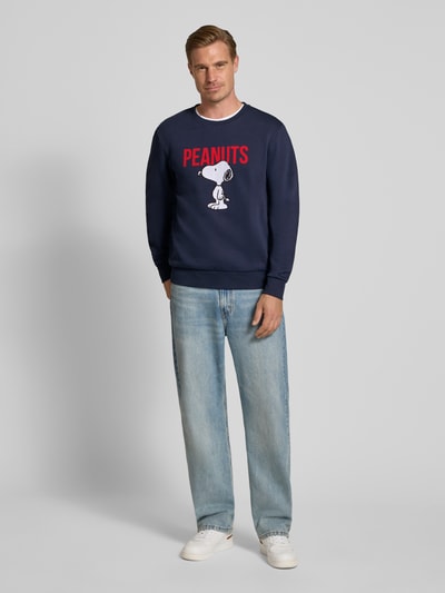Männermodel trägt dunkelblaues Relaxed Fit Sweatshirt aus Baumwoll-Mix von Tom Tailor mit rotem und weißem Print, Ganzkörperansicht von vorne, Herren Sweatshirt von Tom Tailor