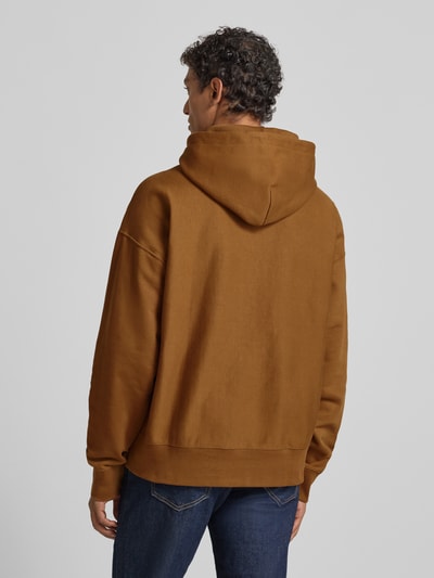 Männermodel trägt Hoodie mit Label-Print und Känguru-Tasche van CK Calvin Klein in bruin, relaxed fit, katoen-elastaan mix, Ganzkörperansicht Rückansicht.