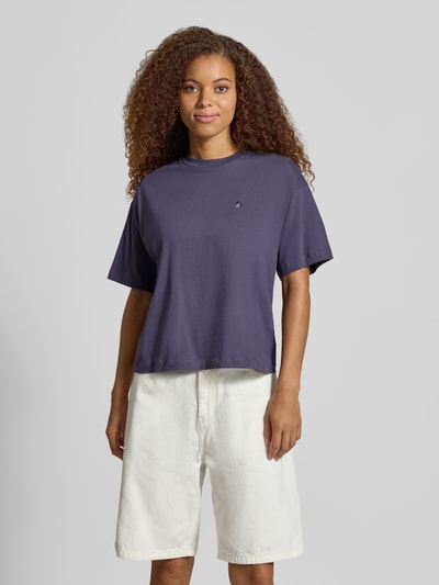 Frauenmodel trägt Regular Fit T-Shirt aus reiner Baumwolle Modell 'CHESTER' von Carhartt Work In Progress, Stehkragen, Halbarm, dunkellila Textur mit kleinem Logo auf der Brust, kombiniert mit weißen Shorts, Ganzkörperansicht von vorne, Damen T-Shirt von Carhartt Work In Progress, Rückenlänge bei Größe S: 56 cm.
