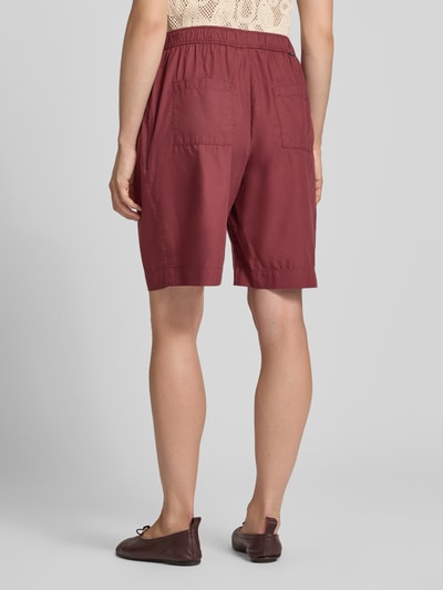 Kobieta nosi Relaxed Fit Bermuda aus reiner Baumwolle od s.Oliver RED LABEL w kolorze bordowym, gładki materiał, widok całej sylwetki z tyłu.