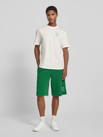 Männermodel trägt weißes Regular Fit T-Shirt aus reiner Baumwolle Modell 'CN Tenniscourt Backprint' von Lacoste, Herren T-Shirt, Ganzkörperansicht von vorne.