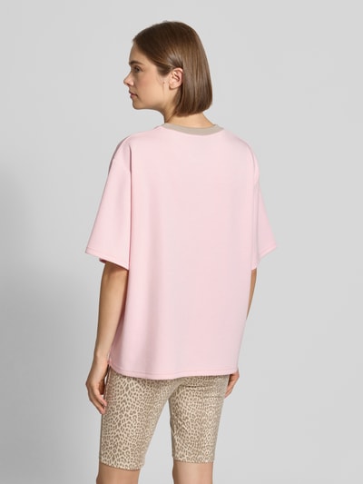 Frauenmodel trägt Trikot mit Label-Print und V-Ausschnitt von OH APRIL in Rosa, Relaxed Fit, glatte Textur, Ganzkörperansicht Rückansicht. Rückenlänge bei Größe S: 62 cm.