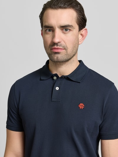 Männermodel trägt Slim Fit Poloshirt mit Logo-Stitching von MCNEAL, reine Baumwolle, Polokragen, dunkelblau, Nahaufnahme Oberkörper.