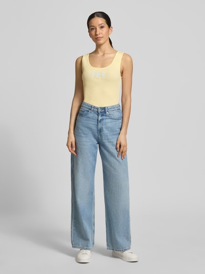Frauenmodel trägt Slim Fit Top mit Logo-Print von GAP in Gelb aus elastischem Baumwoll-Mix mit Rundhalsausschnitt, Ganzkörperansicht von vorne.