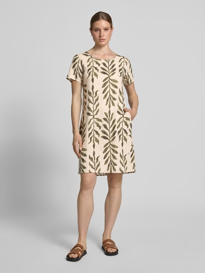 Frauenmodel trägt Relaxed Fit Kleid aus Viskose-Mix Modell 'Tara' von ZABAIONE mit Leinen-Viskose-Anteil, Rundhalsausschnitt, Kurzärmelig, cremefarbene Grundfarbe mit grünem Blätter-Muster, glatte Textur, Rückenlänge 96 cm, Brustweite 49 cm, Ärmellänge 21 cm, Ganzkörperansicht von vorne.