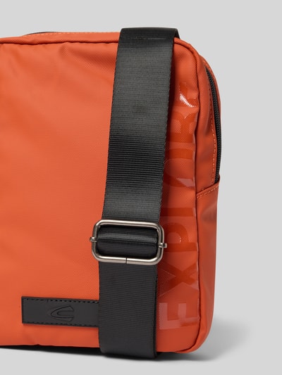 Produktfoto, Crossbody Bag mit Statement-Print Modell 'EXPLORE' von camel active in Orange mit schwarzem Schulterriemen, Nahaufnahme, Kontext: Herren Crossbody Bag mit Hauptfach und Außenfach mit Reißverschluss, verstellbarem Schulterriemen, Maße ca. 19 x 24 x 5 cm, Schulterriemenlänge ca. 112 cm