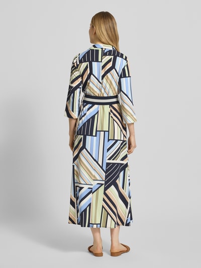 Kobiece modelka nosi Regular Fit Maxikleid in Wickel-Optik od Betty Barclay, wzór geometryczny, niebieski, beżowy, czarny, szalowy kołnierz, dekolt w kształcie V, pasek, rękaw 3/4, długość tyłu w rozmiarze 36: 128 cm, szerokość w rozmiarze 36: 31 cm, długość rękawa w rozmiarze 36: 46 cm, widok całej sylwetki od tyłu.