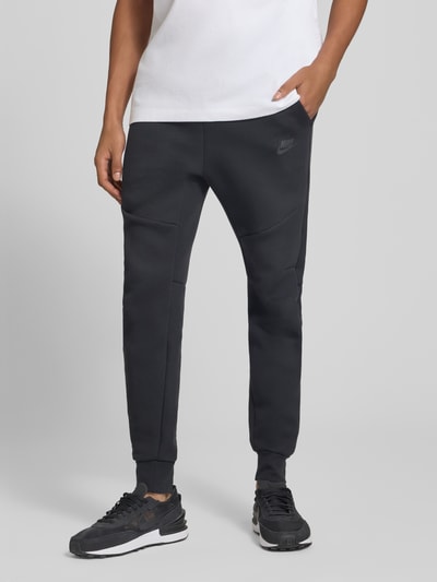 Männermodel trägt Slim Fit Sweathose aus Baumwoll-Mix von Nike in Schwarz, glatte Textur, Herren Sweathose, Ganzkörperansicht von vorne.