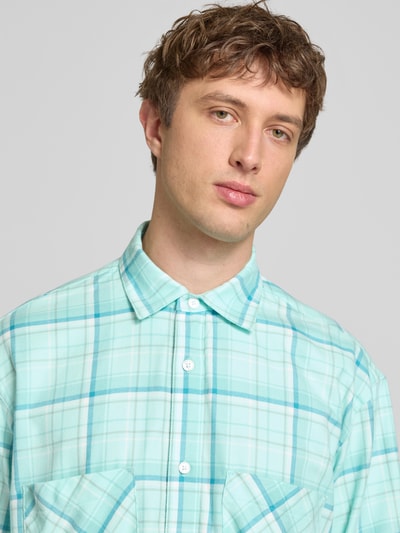 Męski model nosi Modern Fit Freizeithemd mit Brusttaschen Modell 'ACE' od Edwin, bawełna, kołnierzyk kent, kieszenie, krój modern fit, zapięcie na guziki, sportowe mankiety, długość pleców w rozmiarze M: 72 cm, szerokość w rozmiarze M: 55 cm, długość rękawa w rozmiarze M: 60 cm, dominują kolory mięty i błękitu z kratą, tekstura gładka, zbliżenie na górną część ciała