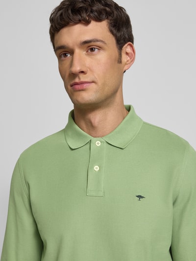Męskimodel nosi Koszulkę polo z wyhaftowanym logo Poloshirt mit Label-Stitching od Fynch-Hatton z bawełny, krój regular fit, kołnierzyk polo, listwa guzikowa, prążkowane zakończenia rękawów, długość tyłu 37 cm w rozmiarze M, kolor jasna zieleń, gładka faktura, nahaufnahme górnej części ciała.