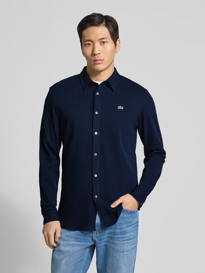 Männermodel trägt Slim Fit Freizeithemd aus reiner Baumwolle von Lacoste in Dunkelblau, Optik: Unifarben, Piqué-Textur, Ganzkörperansicht von vorne.