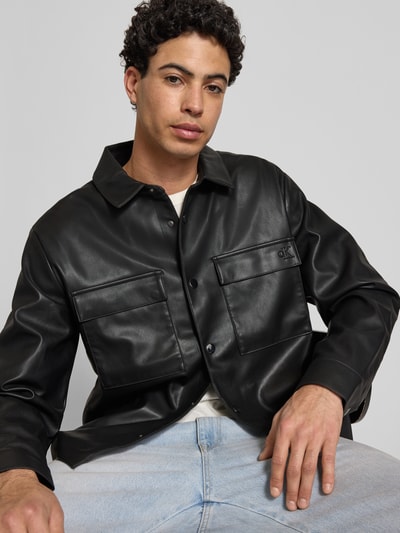 Männermodel trägt Regular Fit Hemdjacke in leerlook van Calvin Klein Jeans, zwart, platte kraag, borstzakken, knoopsluiting, sportmanchet, nahaufnahme oberkörper.