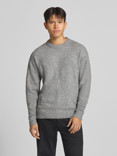 Männermodel trägt grauen Strickpullover mit Rundhalsausschnitt Modell 'SOHO OLLIE' von JACK & JONES, Material-Mix, Ganzkörperansicht von vorne.
