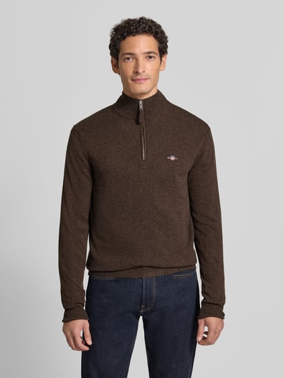 Männermodel trägt Pullover aus reiner Wolle von GANT in Braun, Feinstrick, hochgeschlossener Troyerkragen, Reißverschluss, Ganzkörperansicht von vorne.