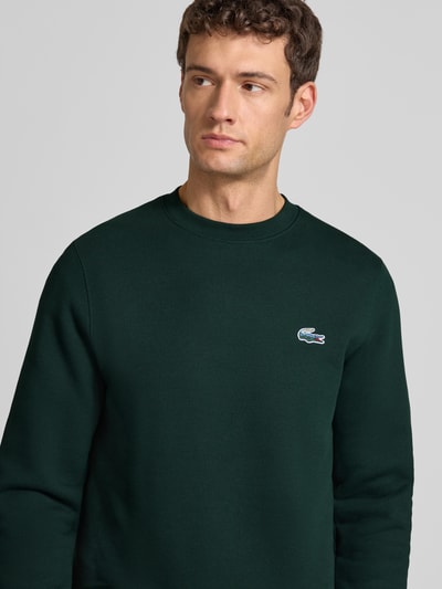 Männermodel trägt Regular Fit Sweatshirt aus reiner Baumwolle von Lacoste, Optik: Unifarben dunkelgrün, Label-Patch, Nahaufnahme Oberkörper.