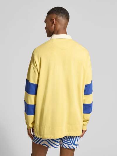 Męski model nosi Relaxed Fit Longsleeve mit Logo-Print od Gant, bawełna, żółty z niebieskimi paskami, polokołnierzyk, długość tyłu 79 cm, długość rękawa 64 cm, widok całej sylwetki od tyłu.