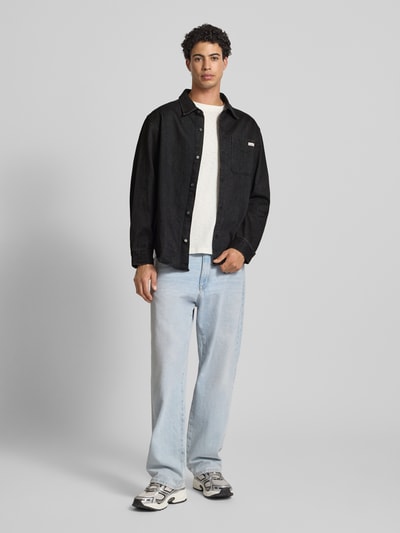 Mannenmodel draagt Regular Fit Jeanshemd met Logo-Patch Modell 'Classic' van Calvin Klein Jeans in zwart, puur katoen, lange mouwen, kentkraag, borstzak, doorlopende knoopsluiting, sportmanchetten, ruglengte maat M 75 cm, frontale full-body weergave.