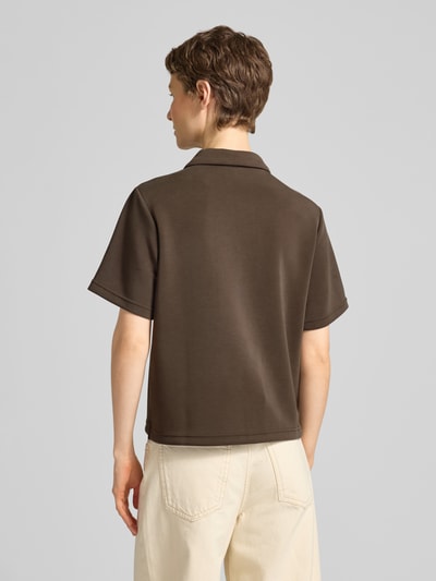Kobiece model prezentuje koszulkę polo Loose Fit Poloshirt mit kurzer Knopfleiste Modell 'Helle' od My Essential Wardrobe, mieszanka materiałów z dodatkiem wiskozy, krój loose fit, kołnierzyk polo, krótka listwa guzikowa, długość tyłu w rozmiarze S: 57 cm, kolor brązowy i kremowy, gładka tekstura, widok całej sylwetki od tyłu.