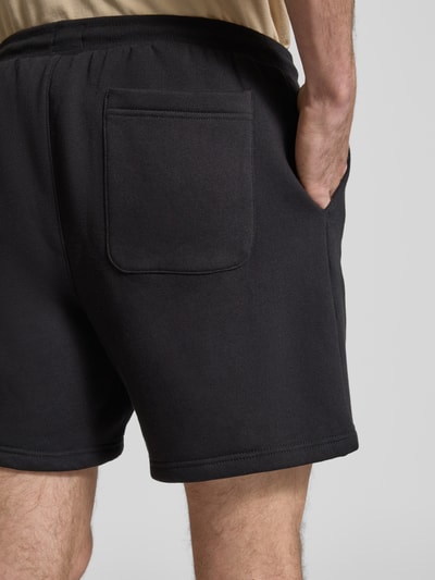 Mężczyznamodel nosi Regular Fit Shorts aus Baumwoll-Mix von Tommy Jeans, efekt: jednolity kolor, detal z logo, tunel, kieszeń z tyłu, dzianina dresowa, mieszanka bawełny, detailaufnahme tyłu.