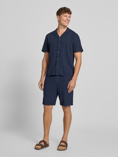 Männermodel trägt Relaxed Fit Stoffshorts aus einer Baumwolle von s.Oliver RED LABEL in Dunkelblau, glatte Textur, Ganzkörperansicht von vorne.