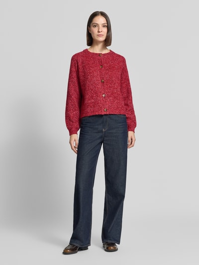 Frauenmodel trägt Relaxed Fit Strickjacke aus Woll-Mix Modell 'Nova' von LOLLYS LAUNDRY in Rot, grobe Textur, lange Ärmel, Ganzkörperansicht von vorne. Damen Strickjacke, durchgehende Knopfleiste, Rückenlänge 52 cm, Ärmellänge 47 cm.