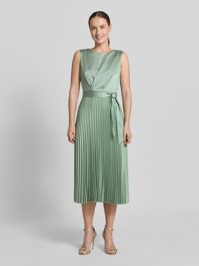 Kobiece modelka nosi sukienkę midi z plisy i wiązanym paskiem 'Midikleid mit Plisseefalten und Bindegürtel' od comma, mieszanka materiałów z dodatkiem streczu, linia a, długość tyłu w rozmiarze 36: 35 cm, szerokość w rozmiarze 36: 40 cm, jasna zieleń, wyraźna tekstura plisów, widok całej sylwetki z przodu.