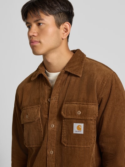 Männermodel trägt Regular Fit Hemdjacke aus Cord Modell 'WHITSOME' von Carhartt Work In Progress, braun, sichtbare Textur, Nahaufnahme Oberkörper. Reine Baumwolle, Umlegekragen, Brusttaschen mit Label-Patch.