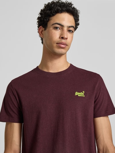 Männermodel trägt Regular Fit T-Shirt mit Logo-Stitching von Superdry in Bordeaux, reine Baumwolle, Rundhalsausschnitt, Nahaufnahme Oberkörper.