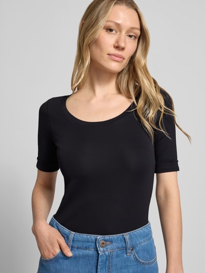 Kobiece modelka nosi T-Shirt mit Ärmelaufschlag und Rundhalsausschnitt von Marc Cain, mieszanka bawełny z dodatkiem streczu, dopasowany krój, okrągły dekolt, zakładka na rękawach, detal z logo, długość tyłu w rozmiarze 36: 60 cm, ciemny kolor, gładka tekstura. Zbliżenie na górną część ciała, widok z przodu.
