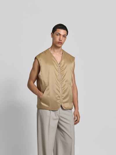 Männermodel trägt Relaxed Fit Weste in Stepp-Optik von MM6 Maison Margiela in Beige mit Eingrifftaschen, V-Ausschnitt, Reißverschluss, Ganzkörperansicht von vorne.
