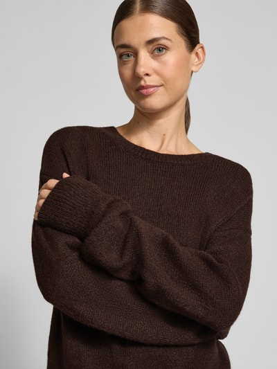 Vrouwenmodel draagt Oversized Fit Strickpullover mit Rundhalsausschnitt van Milano Italy in donkerbruin, gebreide structuur, elastische materiaalmix, geribde randen, lange mouwen, damestop, detailopname bovenlichaam.
