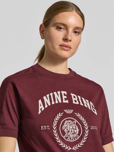 Vrouwenmodel draagt t-shirt met labelprint van Anine Bing, puur katoen, recht model, ronde hals, ruglengte maat S: 58 cm, detailopname bovenlichaam.
