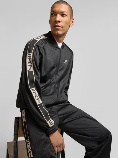 Männermodel trägt schwarze Trainingsjacke mit Zweiwege-Reißverschluss von EA7 Emporio Armani, Logo, Stehkragen, Regular-Fit, Nahaufnahme Oberkörper.