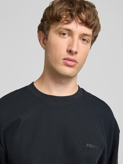 Męski model nosi Relaxed Fit T-Shirt mit Strukturmuster od REVIEW, czarny, bawełna, okrągły dekolt, długość tyłu 67 cm, Nahaufnahme górnej części ciała.