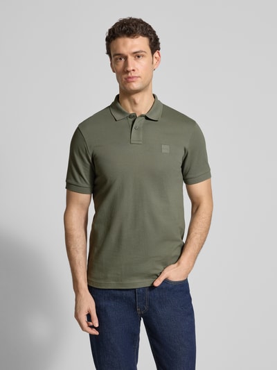 Männermodel trägt Slim Fit Poloshirt aus Baumwoll-Mix Modell 'PASSENGER' von BOSS Orange in Olive, Label Patch, Ganzkörperansicht von vorne.