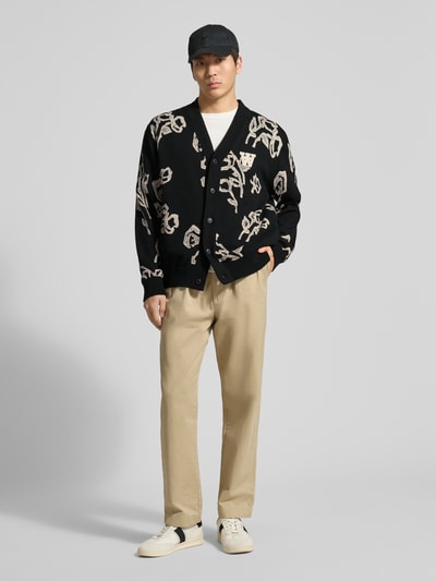 Męski model nosi Cardigan im Allover-Look Modell 'Leif' od Wood Wood z czystej bawełny organicznej, krój regular fit, czarno-beżowy wzór, zapięcie na guziki, przód w pełnym widoku.