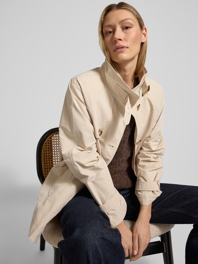 Vrouwenmodel draagt Trenchcoat met Stehkragen und Ärmelriegeln van Fuchs Schmitt in regular fit, lichte beige kleur, met knoopsluiting, steekzakken en mouwriemen, schouderbreedte 36 cm, borstwijdte 56 cm, mouwlengte 53 cm, ruglengte 72 cm, detailopname bovenlichaam.