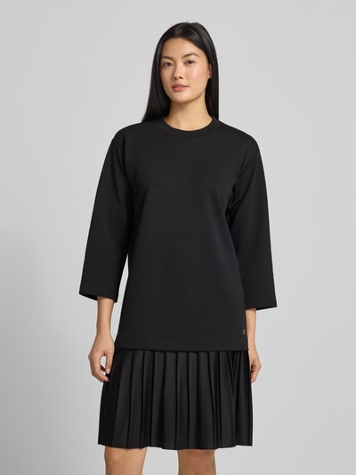 Kobiece model prezentuje sukienkę Knielanges Kleid im 2-in-1-Look Modell 'Tarika' od JOOP!, czarna, krój relaxed fit, długość do kolan, okrągły dekolt, rękaw o dł. 3/4, długość tyłu 95 cm, szerokość klatki piersiowej 51 cm, długość rękawów 46 cm, faktura gładka z plisowanym dołem, całkowity widok z przodu.